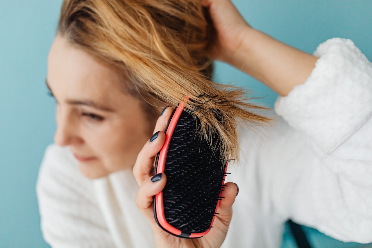 Close-up of a woman brushing her blonde hair with a red hairbrush indoors.