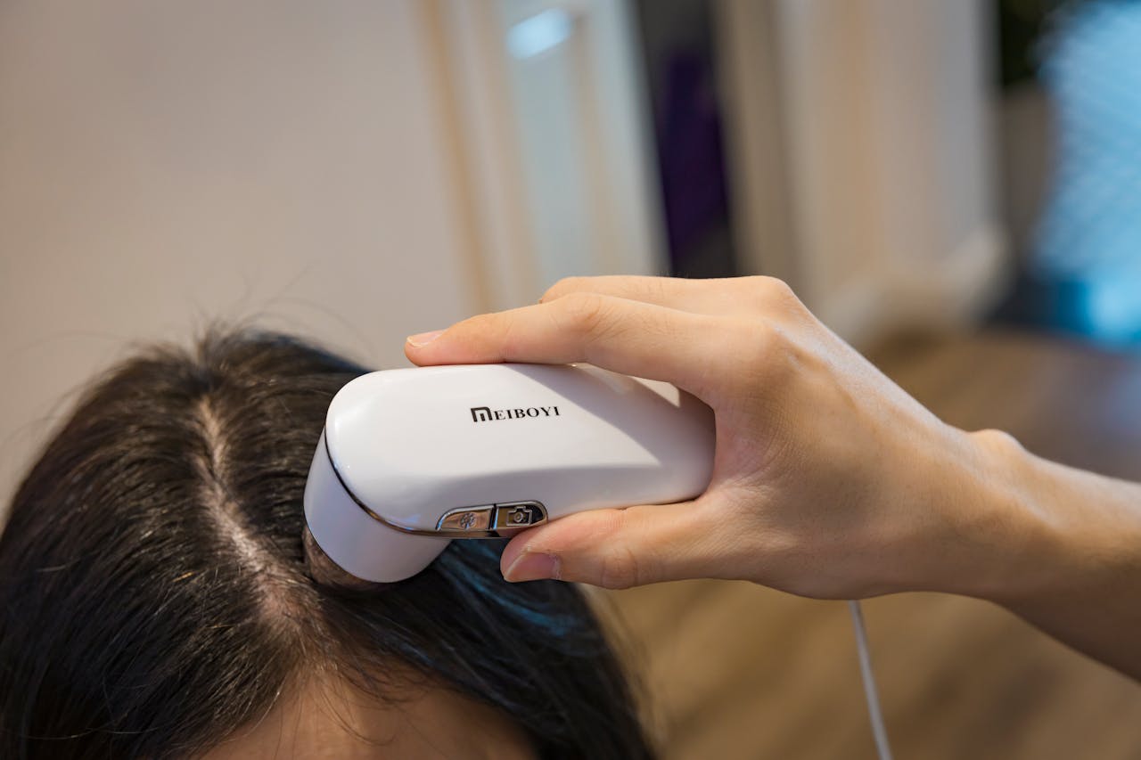 Close-up of a handheld device examining a persons scalp indoors.